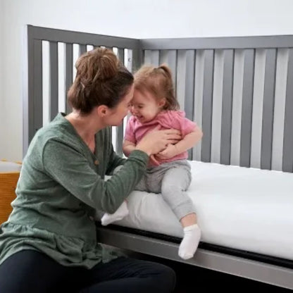 Mother and toddler sitting on a crib with a Modugreen Baby Gentle Start Breathable Cover featuring a blue leaf print.