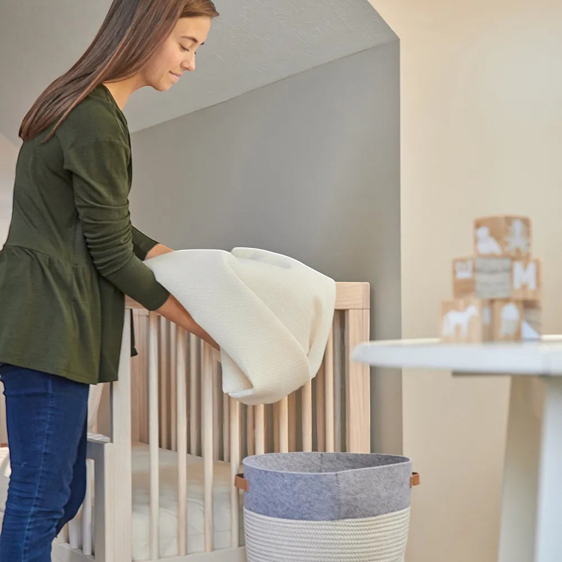Modugreen Baby breathable crib mattress cover made of organic cotton and 3D mesh, held by a woman in a nursery.