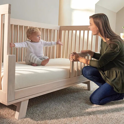 Modugreen Baby breathable crib mattress cover with organic cotton surface on a wooden crib with a mother and baby.