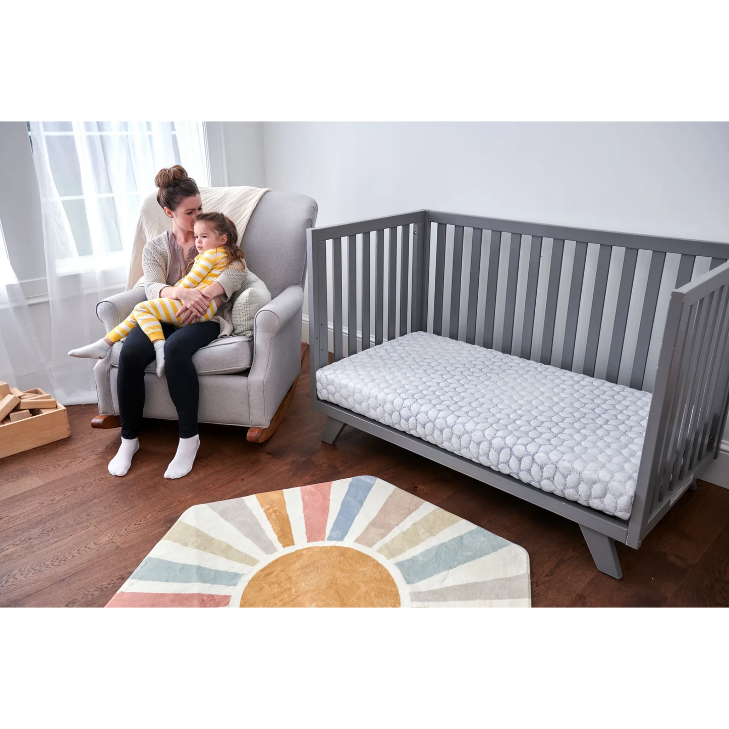 Modugreen Baby Gentle Start breathable crib mattress with 3D lattice cover in a grey crib, next to a mother and child.