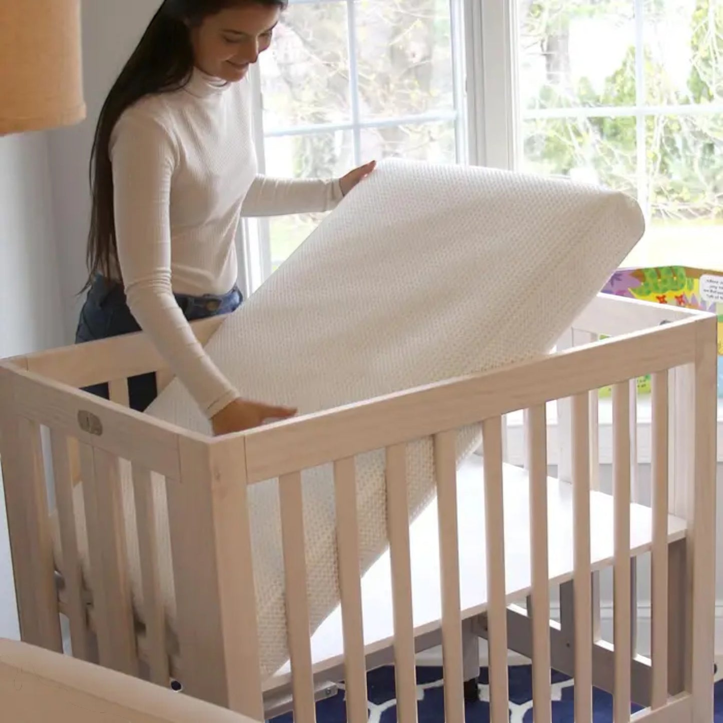 Modugreen Baby Breathe-Safe mini crib mattress with a white 3D breathable cover being placed into a wooden crib.