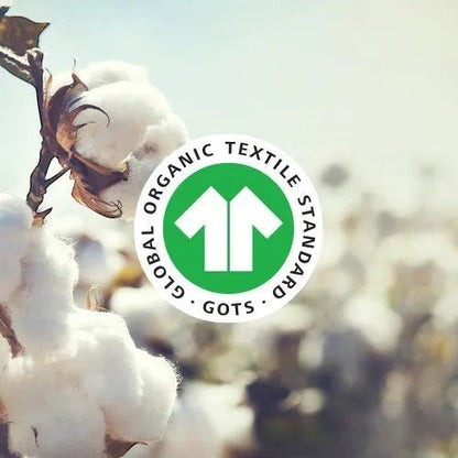 Modugreen Baby GOTS certified organic cotton symbol overlaid on a soft-focus field of raw organic cotton plants.