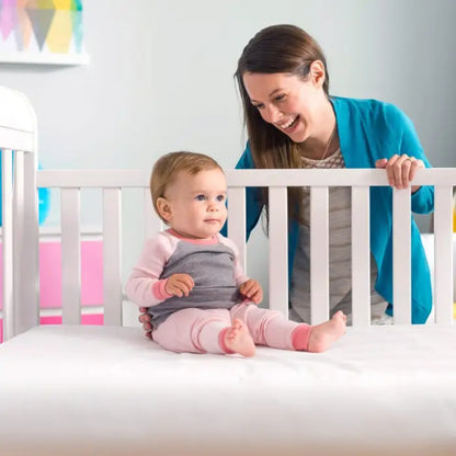 Modugreen Baby Lullaby Earth crib mattress with a happy baby sitting on the firm, white surface in a nursery.