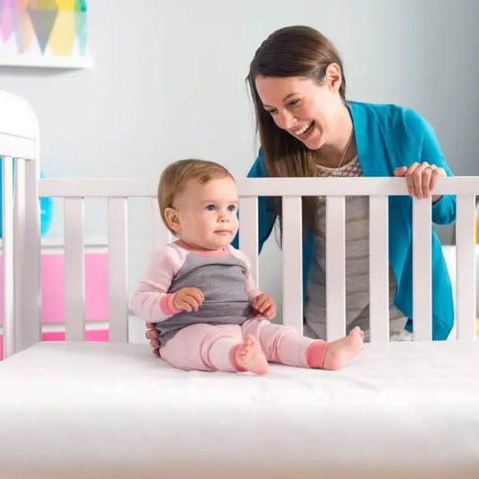 Modugreen Baby Lullaby Earth crib mattress with a happy baby sitting on the firm, white surface in a nursery.