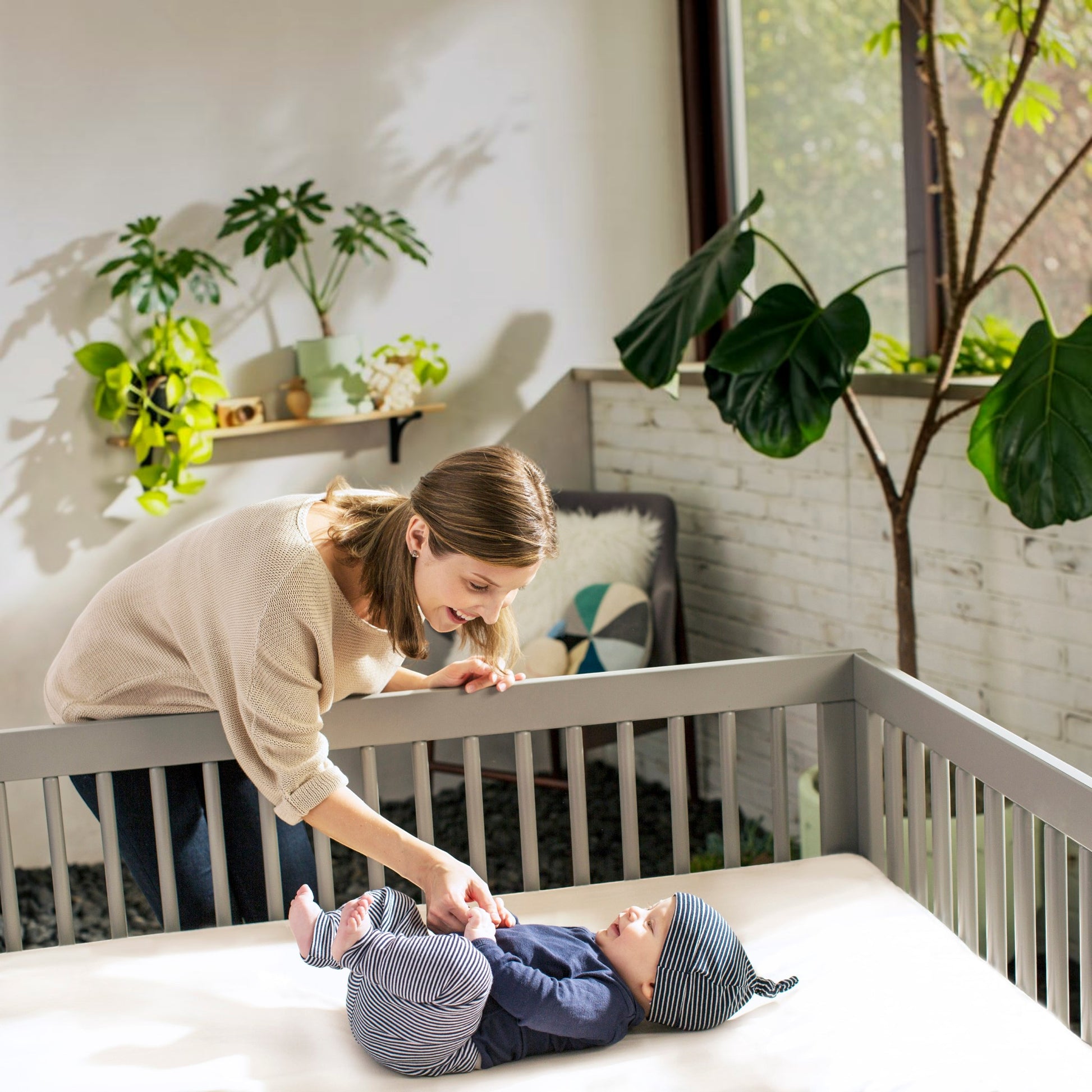 Modugreen Baby organic cotton crib mattress in a bright nursery with a mother smiling at her baby lying on the bed.