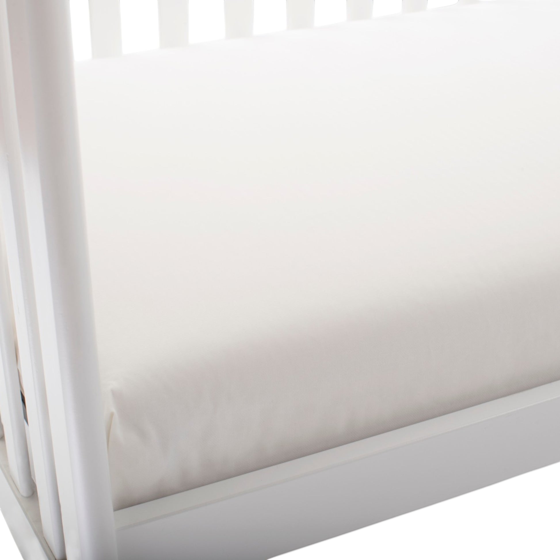 Modugreen Baby organic cotton 2-stage crib mattress with a smooth white surface inside a white wooden crib frame.