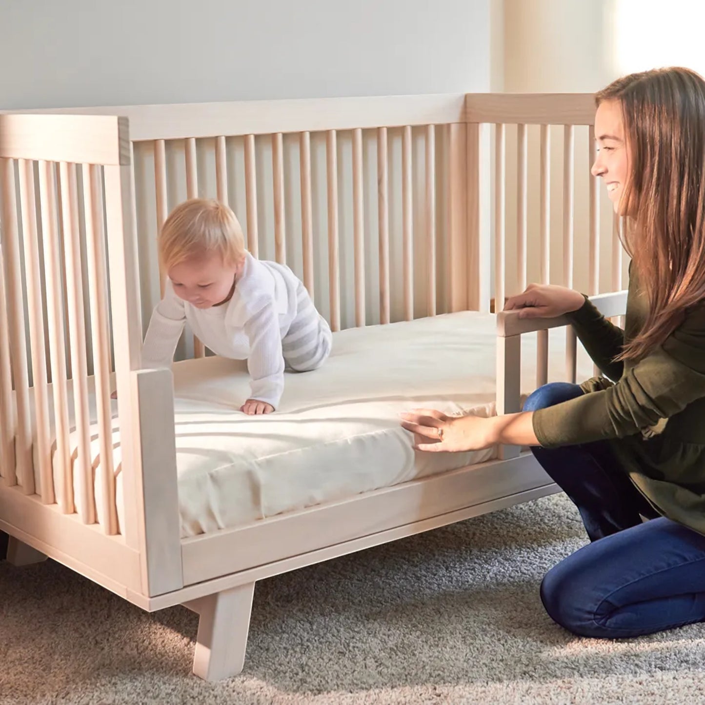 Modugreen Baby organic cotton flat crib mattress protector pad on a wooden crib with a baby and mother.