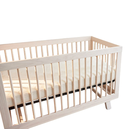 Modugreen Baby breathable organic 2-stage crib mattress with quilted cover inside a light wood slatted crib