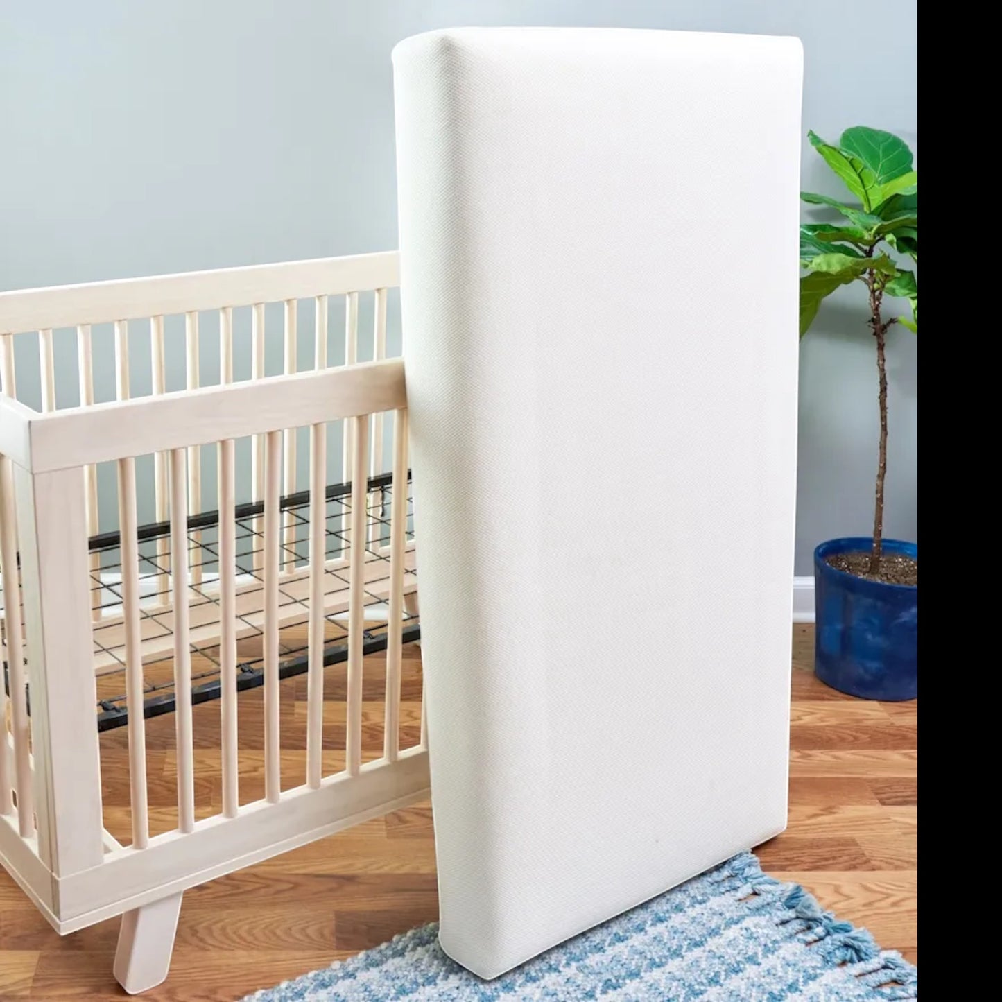 Modugreen Baby organic 2-stage innerspring crib mattress with breathable white 3D mesh cover next to a wooden crib.