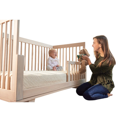 Modugreen Baby 2-stage organic crib mattress with quilted cover in a wooden crib with a smiling baby and mother.