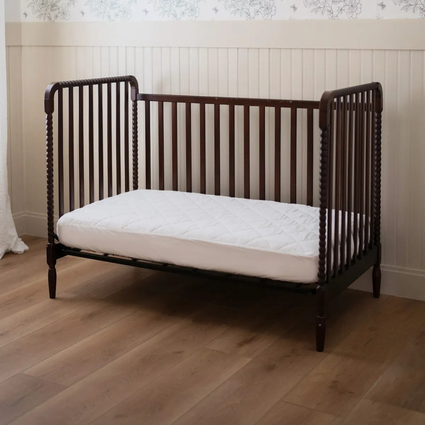 Modugreen Baby organic quilted waterproof crib mattress protector pad in white, fitted on a dark wood spindle crib.