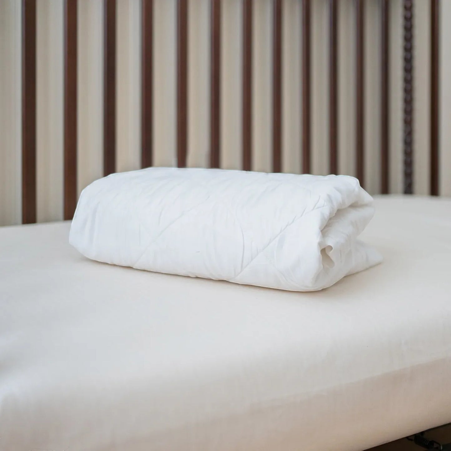 Modugreen Baby organic quilted waterproof crib mattress protector pad in white, folded on a wooden crib mattress.