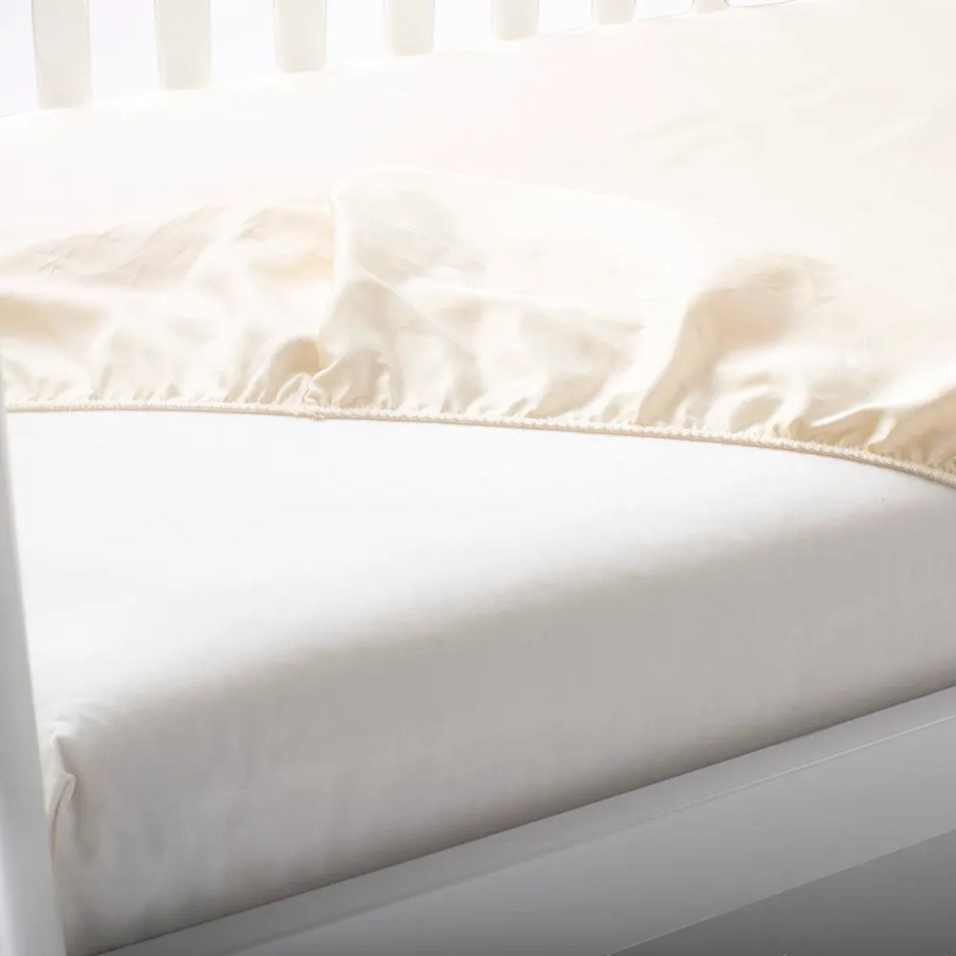 Modugreen Baby ivory organic cotton sateen crib sheet with a smooth 300 thread count fitted on a white crib mattress.
